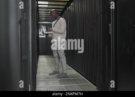Server room, data center or IT black man with laptop for research, engineer working in dark server room. Computer, cybersecurity and analytics with Stock Photo