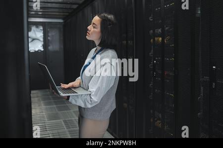 Server room, laptop and young woman or technician in data center management, system and cyber security. Thinking, serious and inspection of asian Stock Photo