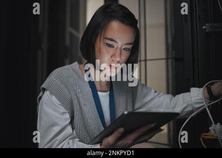 Tablet, server room and communication with a programmer asian woman at work on a computer mainframe. Software, database and information technology Stock Photo