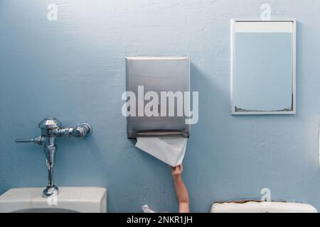 Child reaching for paper towel from dispenser in public washroom Stock Photo