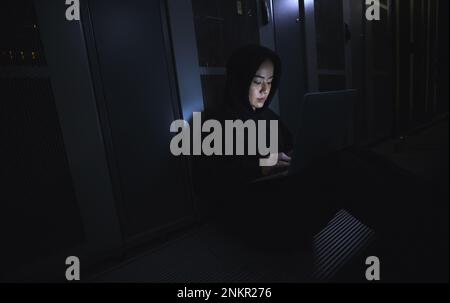 Hacking, laptop and hacker woman in dark server room for coding software, data center crime or cyberpunk intel. Network criminal, person or user in Stock Photo
