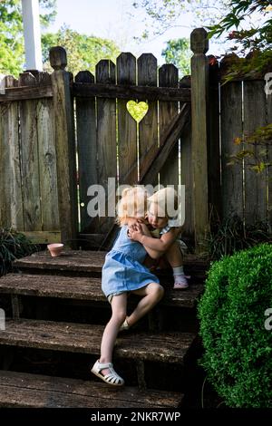 Two girls hugging on wooden steps in back yard Stock Photo