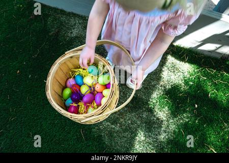 Overhead of girl carrying basket with colorful painted Easter eggs Stock Photo