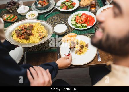 Muslim woman putting pilaf on plate near blurred husband at home,stock image Stock Photo