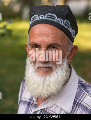 Dushanbe, Tajikistan - 08 20 2019 : Outdoor portrait of bearded Tajik old man wearing traditional ethnic black skull cap Stock Photo