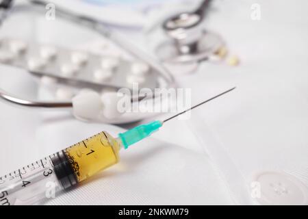 close-up of a syringe loaded with medication. in the background: pills, stethoscope and doctor's gown. Stock Photo