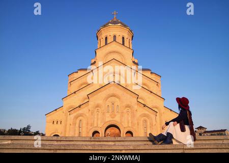 Female Visitor Sitting on the Staircase of the Holy Trinity Cathedral of Tbilisi or the Sameba, Tbilisi, Georgia Stock Photo