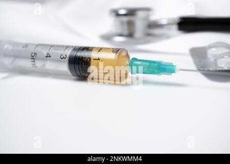 close-up of a syringe loaded with medication with a stethoscope in the background on a white background Stock Photo