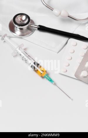 close-up of a syringe loaded with medication. in the background: pills, stethoscope and doctor's gown. Stock Photo