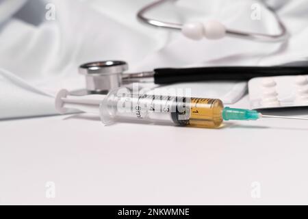 close-up of a syringe loaded with medication. in the background: pills, stethoscope and doctor's gown. Stock Photo