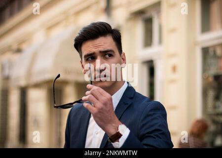 Portrait of an attractive young businessman holding sunglasses on the street Stock Photo