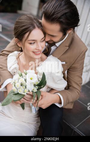 overhead view of bearded groom hugging smiling bride in white dress with wedding bouquet,stock image Stock Photo