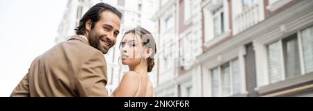 happy groom in beige suit smiling near gorgeous bride outdoors, banner,stock image Stock Photo