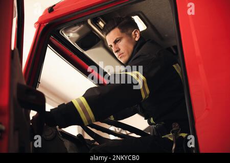 Firefighter sitting in fire truck at station, low angle view Stock Photo