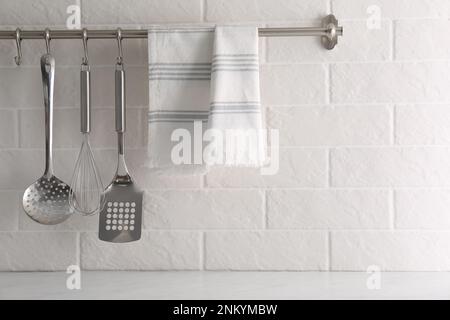 Soft kitchen towel and utensils hanging on rack near white brick wall Stock Photo