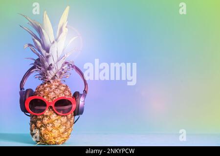 Pineapple with headphones and sunglasses on color background, space for text. Summer party Stock Photo