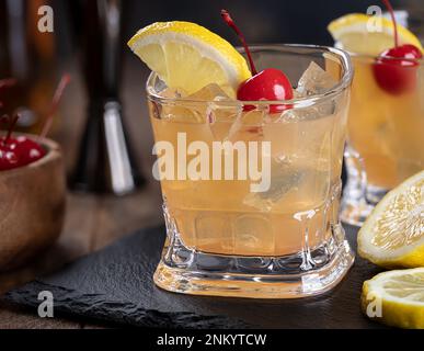 Whiskey sour cocktail with marachino cherry and lemon slice on black slate board Stock Photo