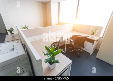 Professional office space with multiple desks and chairs, along with several potted plants, in a bright and airy room Stock Photo