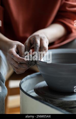 Artisan woman hands shaping deep plate made of natural clay placed on spinning potter whee Stock Photo