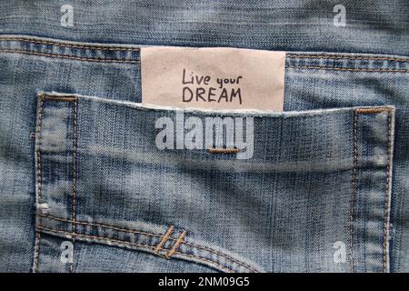 Live your dream concept. Motivational quotes inscription on a tag in a pocket of blue jeans. Stock Photo