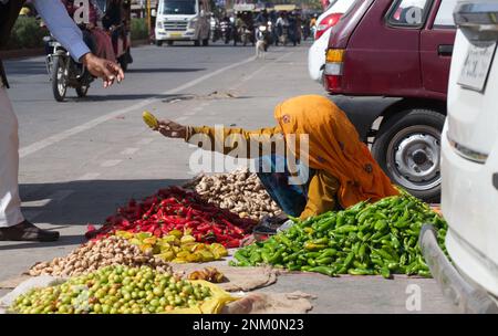 An elderly women in bright traditional clothing selling fruits and vegetables from the street in Jaipur, India Stock Photo