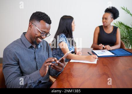 Black businessman smiles while using digital tablet at conference table meeting Stock Photo