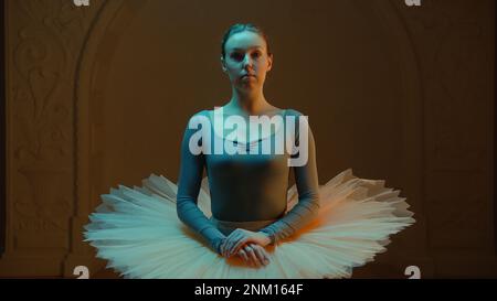 Cinematic shot of elegant ballerina in ballet tutu standing in opera lobby after choreography rehearsal, looking at camera. Beautiful ballet dancer before performance in theater. Classical ballet art. Stock Photo