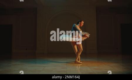 Cinematic shot of beautiful classical ballet female dancer in white tutu dress dancing in theatre lobby and preparing to start the performance. Choreography before start of show. Classical ballet art. Stock Photo