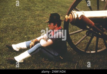 1970s America: Old time rifleman's meet, June 24, 1973, is held on the Greenfield Village green adjoining the Henry Ford Museum of Dearborn. A 'soldier' rests against an old brass cannon Stock Photo