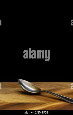 Old vintage spoon on top of a wooden board with black background, copy space. Stock Photo