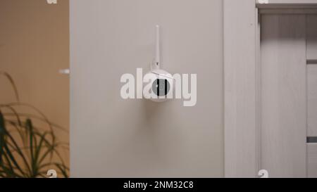 Installed security camera on the wall in the modern apartment. CCTV camera with microphone and motion sensor. Concept of monitoring system, surveillance, safety and personal privacy. Stock Photo