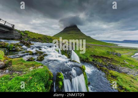 Beautiful moody clouds over Kirkjufell mountain and waterfall flowing in summer at Iceland Stock Photo