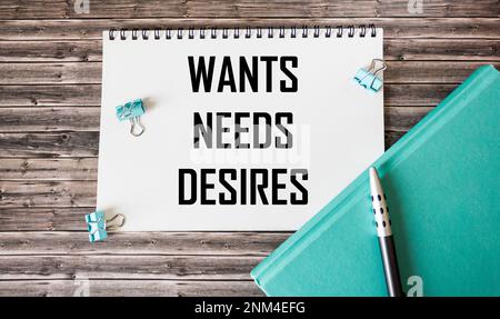 Symbol of needs and desires. Word concept Wants Desire needs on wooden blocks. On a wooden table is a green diary and a pen. Business, psychological a Stock Photo