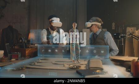 Two multi ethnic tailors in VR headsets in atelier. 3D female hologram of garment pattern. Virtual interface menu of program for designing and modeling clothes. Concept of AR modern technologies. Stock Photo