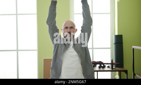 Young bald man standing with relaxed expression stretching arms at sport center Stock Photo