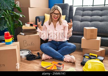 Young hispanic woman moving to a new home sitting on the floor shouting with crazy expression doing rock symbol with hands up. music star. heavy music Stock Photo