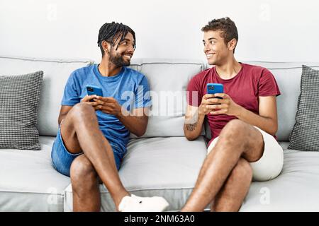 Two men friends using smartphone sitting on sofa at home Stock Photo