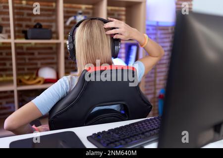 Young caucasian woman playing video games wearing headphones backwards thinking about doubt with hand on head Stock Photo