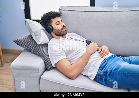 Young arab man listening to music sleeping on sofa at home Stock Photo