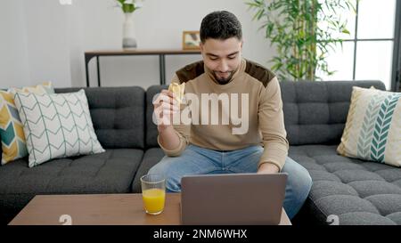 Young arab man having breakfast using laptop at home Stock Photo
