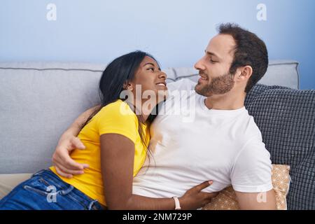 Man and woman interracial couple hugging each other lying on sofa at home Stock Photo