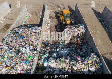 Skid steer loader moving plastic garbage with scrap grapple on the landfill site, drone shot. Waste disposal concept. Stock Photo