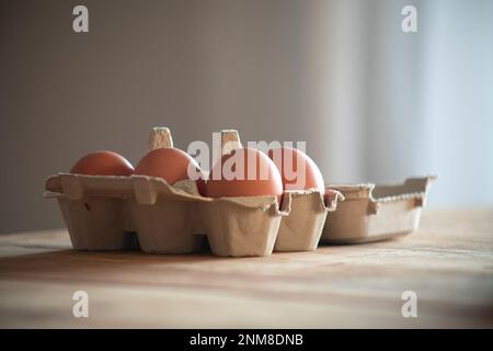 Half dozen eggs in a carton box on naturally lit wooden table Stock Photo