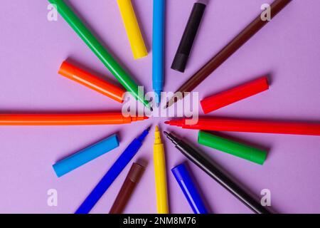 Felt-tip pens without caps of different colors on a purple background. Arranged in a circle. Stock Photo
