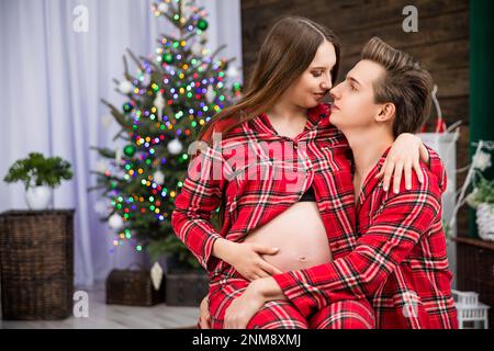 A pregnant woman sits on her husband's lap and embraces him tenderly. Stock Photo