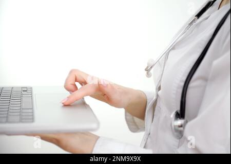 Close up woman doctor working on laptop, typing on keyboard, therapist physician nurse sitting at work table in hospital office, using medical apps, consulting online, writing report. High quality  Stock Photo