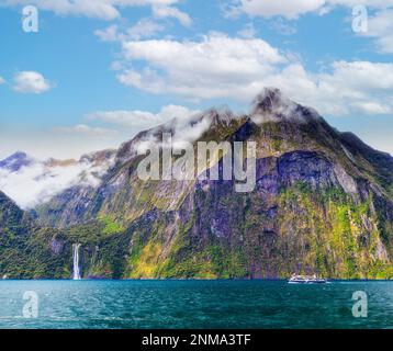 Milford Sound mountain peaks and scenic waterfalls in New Zealand with passenger tourist cruise boat at Stirling fall. Stock Photo