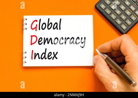 GDI global democracy index symbol. Concept words GDI global democracy index on white note on beautiful orange background. Businessman hand. Business a Stock Photo