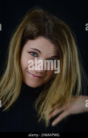portrait of a beautiful smiling blonde woman arranging her hair in motion with her hand Stock Photo