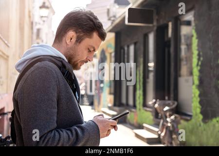 Man standing on street and using his phone, typing text, online messaging. Stock Photo